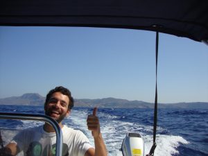 Man Smiling and Driving Boat on the Water with Mountains in Background